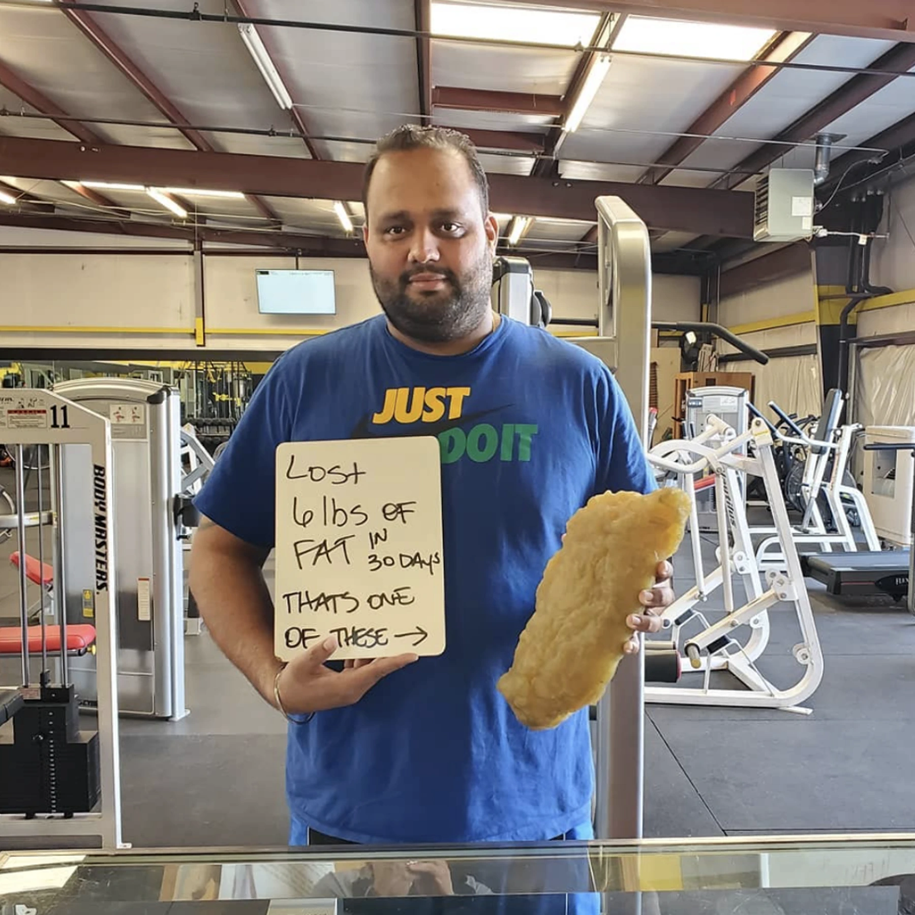 Client in an FGP shirt holding a board that reads I lost 6 lbs of fat in 30 days, in front of a Fitness Grind and Performance backdrop.